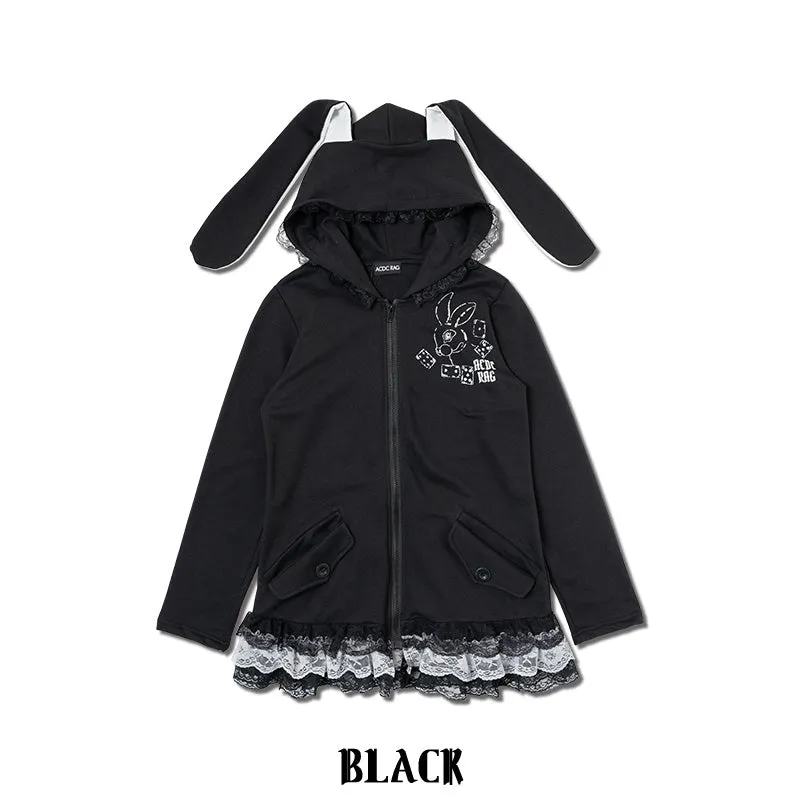 Product photograph: a black zip hoodie with long white-lined rabbit ears on the hood, a white rabbit-and-dice print on the chest, and a black lace frill along the hem, on a white background.