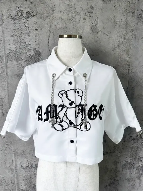 A short white shirt with gothic lettering and a bear graphic, shown on a dress form with no person in the frame.