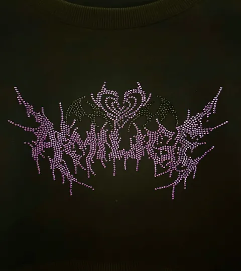 Pale pink rhinestones set into black fabric, spelling the brand name in an angular gothic hand.