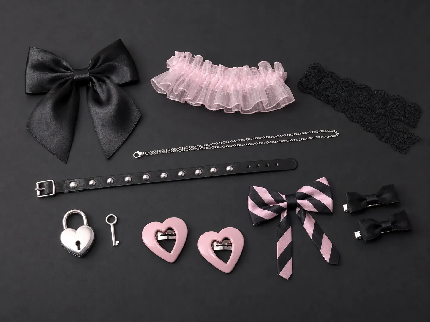 Generated editorial image: black and baby pink accessories on a dark charcoal surface — a large black satin bow, a pink organza frill, a black lace band, a fine silver chain, a black leather belt set with silver studs, a heart-shaped silver padlock with a key, two pink heart hair clips, a black and pink striped bow, and two small black bow clips.
